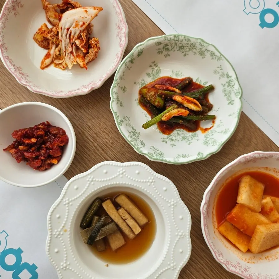 Side dish spread at Aewol Eomma including kimchi and garlic scape pickles