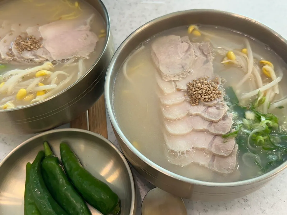 Two bowls of bone-broth pork noodle soup with dombe naengsuyuk on the table