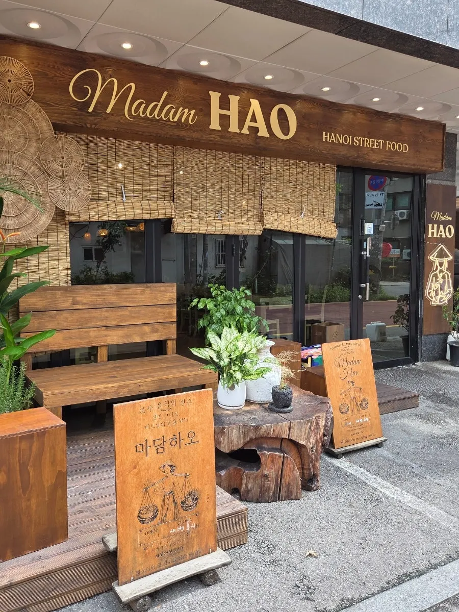 Madam Hao's exterior with a wood-toned sign and plants