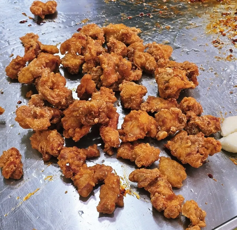 Dakgangjeong being tossed with sauce on the sizzling pan