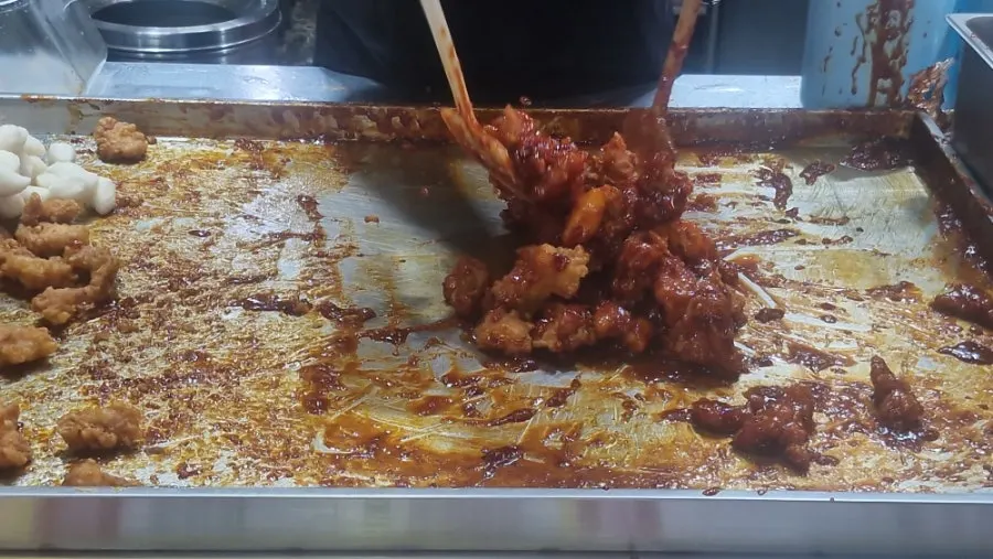 Dakgangjeong being tossed in the ordered sauce
