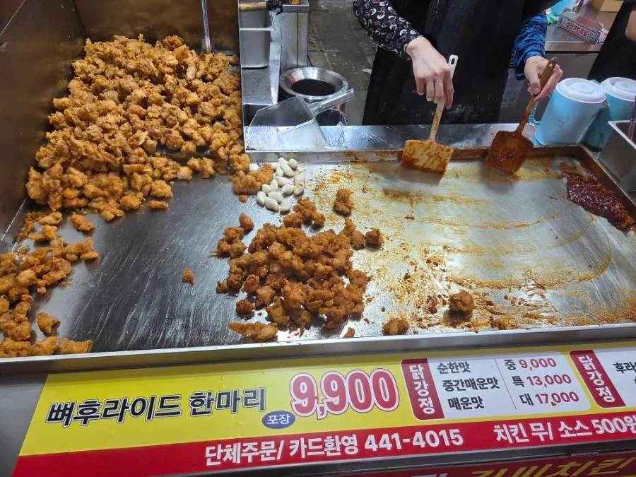 Kitchen staff tossing dakgangjeong in sauce on a flat pan