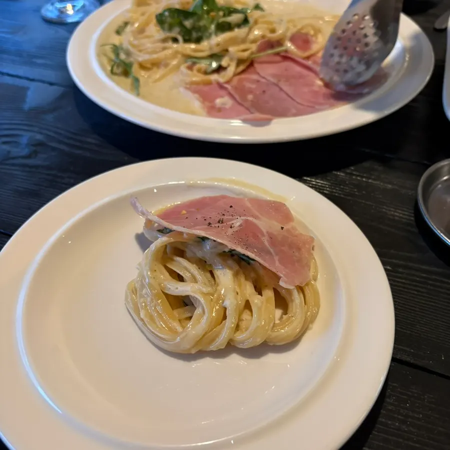 Close-up of cream pasta topped with jambon and arugula