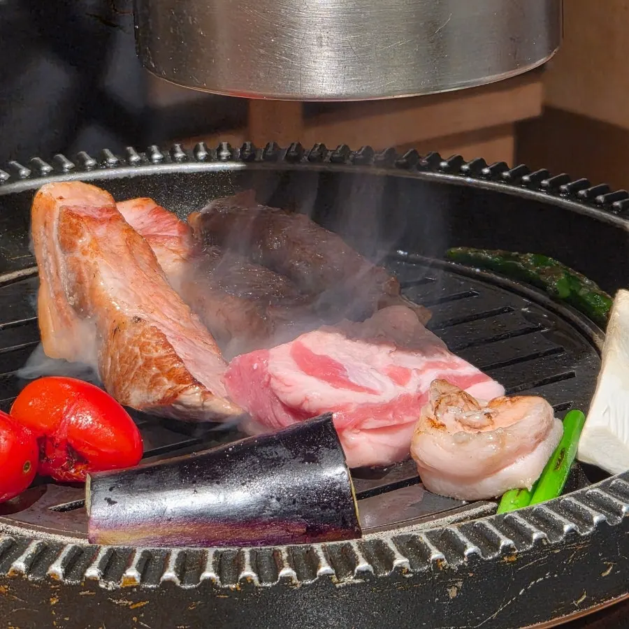 Pork neck grilling alongside vegetables on the grill