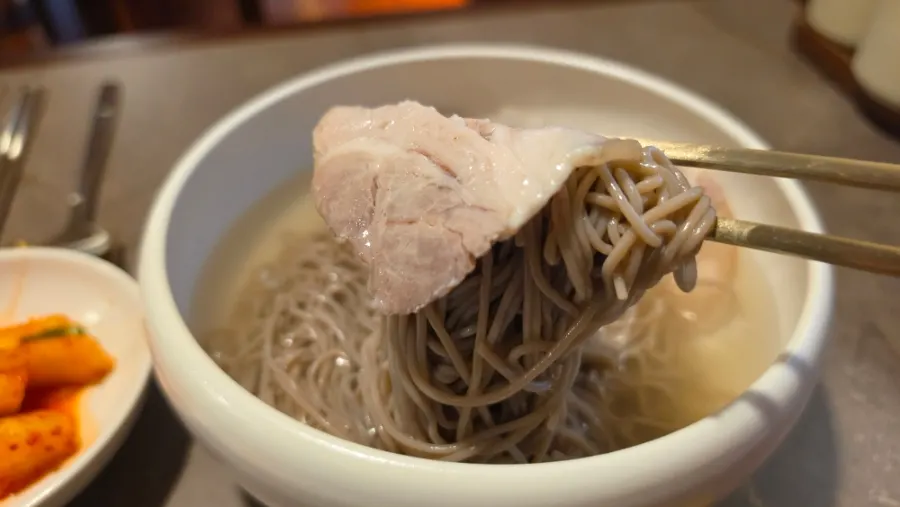 A bite of buckwheat naengmyeon wrapped around boiled pork