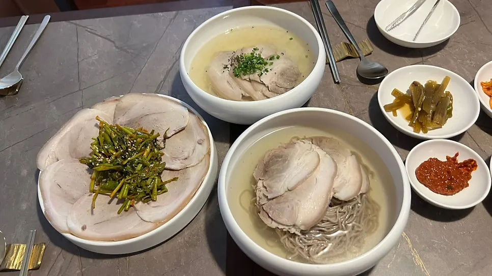Full table set with clear gomtang, Pyongyang naengmyeon and warm pork