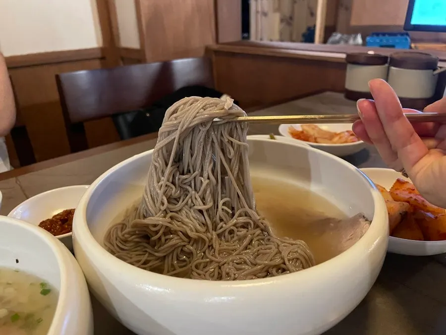 Chewy naengmyeon noodles lifted with chopsticks