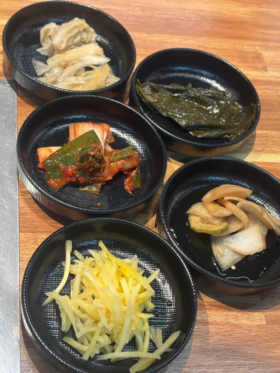 Spread of side dishes including pickled onion and green onion kimchi typical of eel restaurants