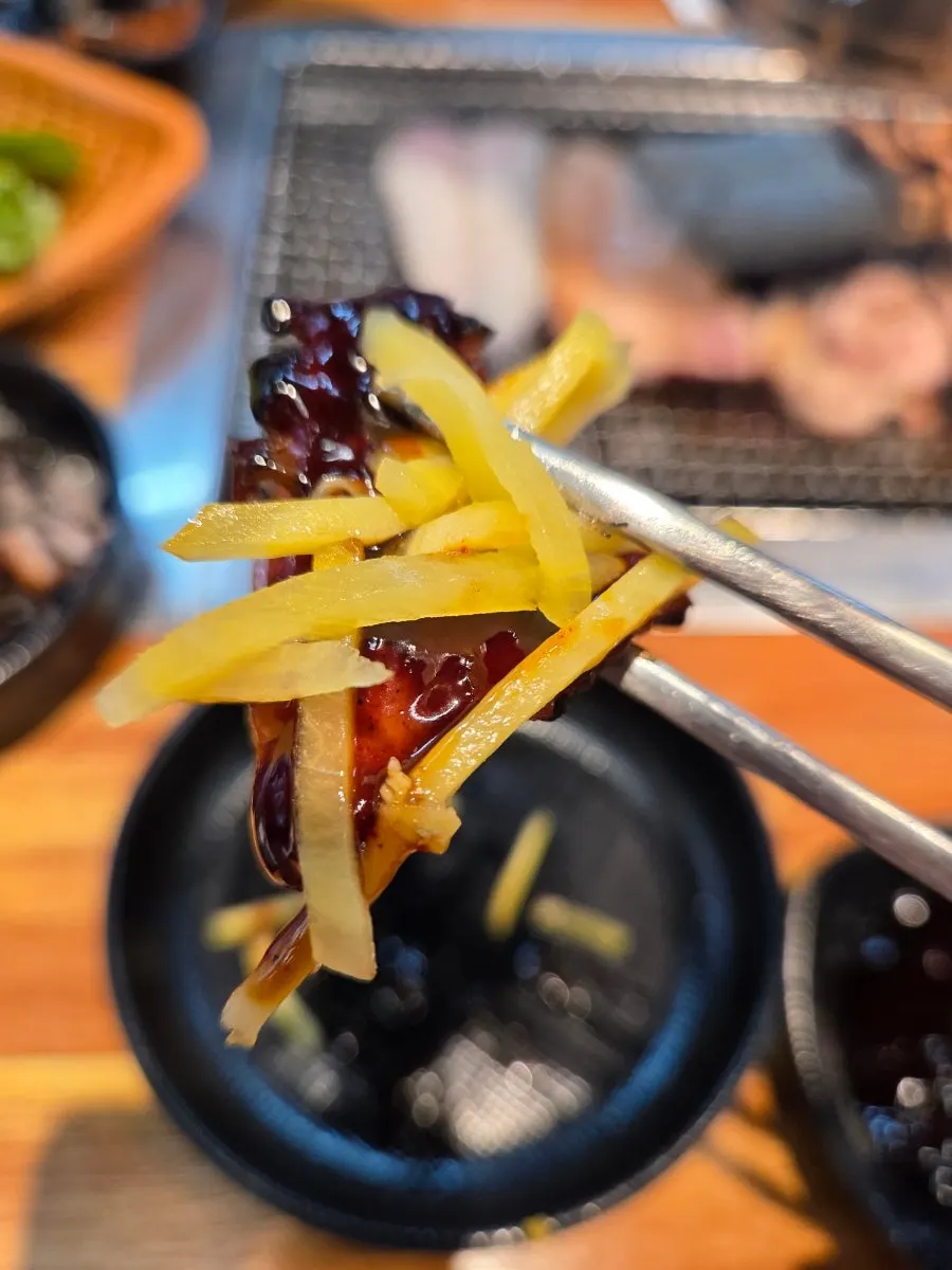 A piece of grilled eel topped with ginger strips
