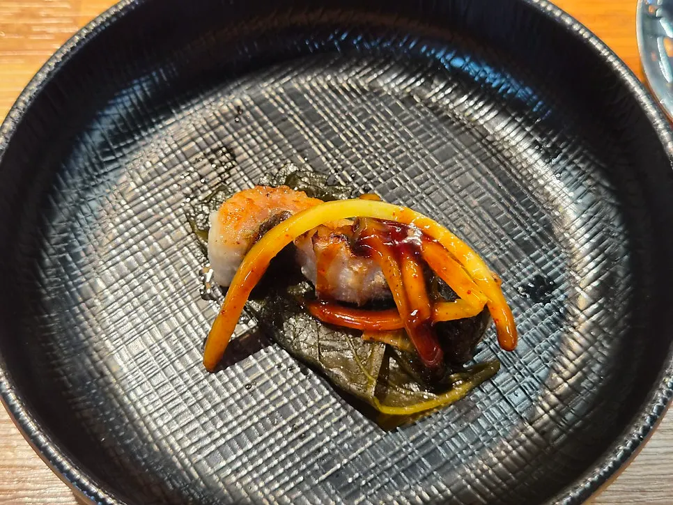 A piece of eel topped with ginger on pickled perilla leaf