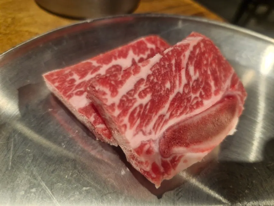 Aged LA galbi, half raw and half marinated, on the grill