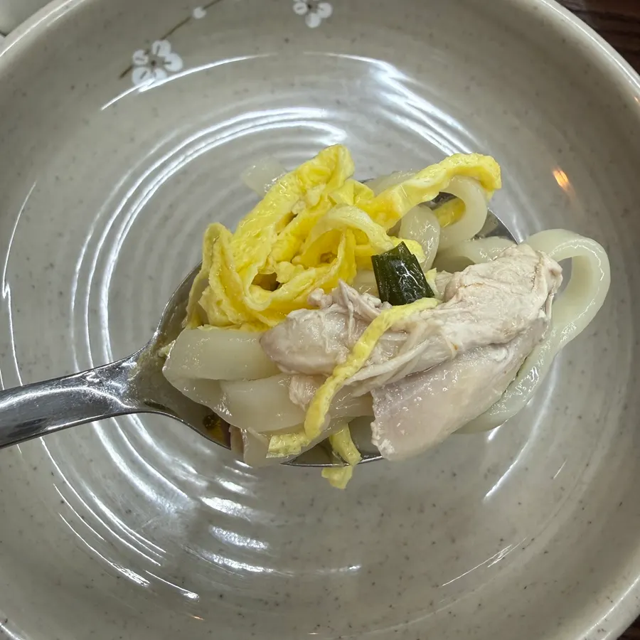 A bite of chicken kalguksu with egg garnish and chicken