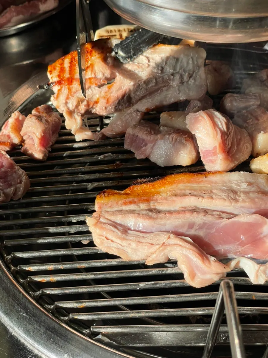 Four slices of pork belly cooking on the grill