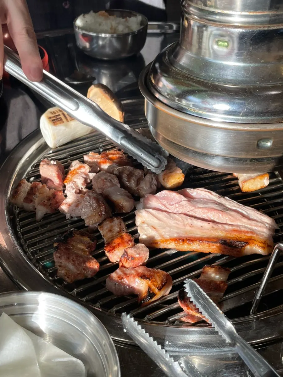 Thick pork belly grilling alongside king oyster mushrooms