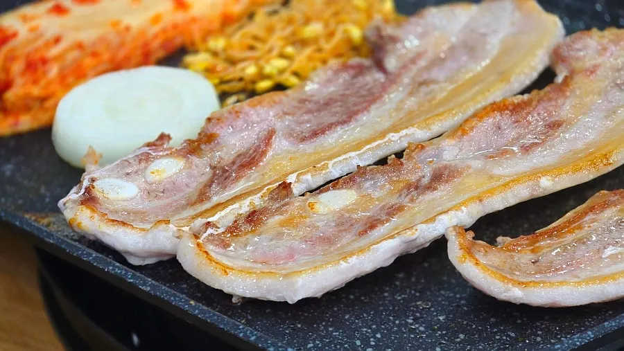 Pork belly and onion cooking on the grill