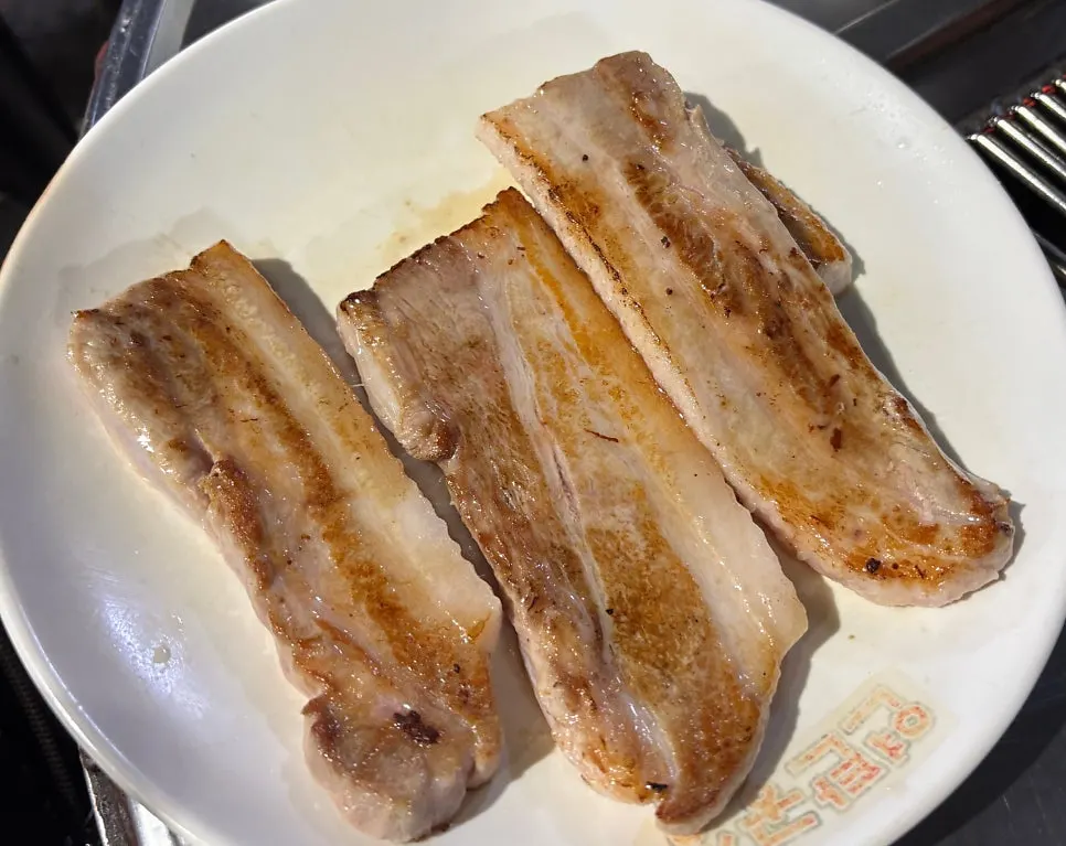 Partially grilled pork belly cooking over charcoal