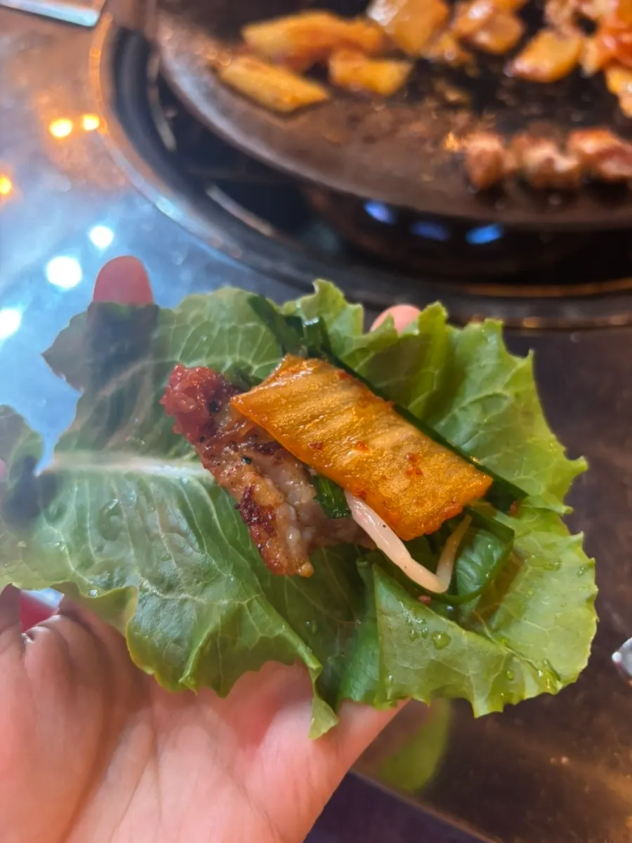 A pork belly wrap topped with seasoned bean sprouts and aged kimchi