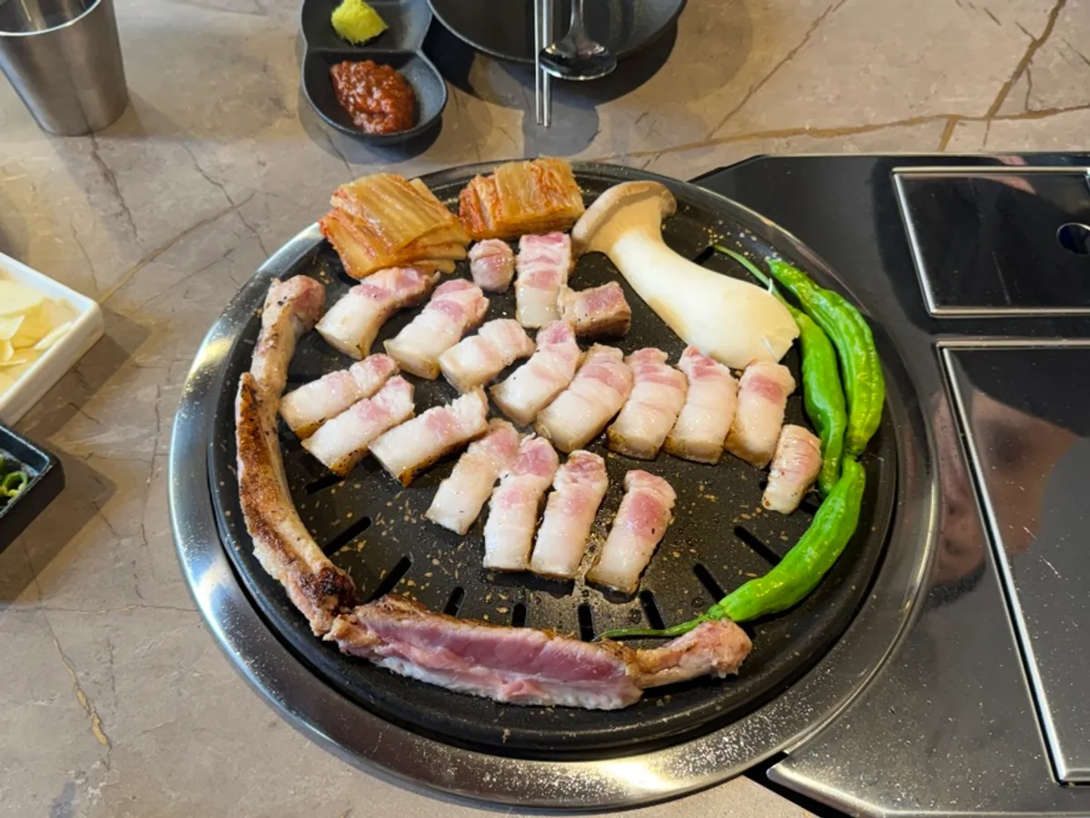 A staff member grilling bone samgyeopsal and vegetables