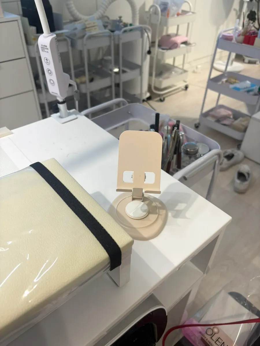 Hands receiving nail prep with a phone stand set up nearby
