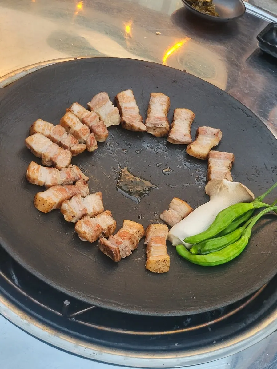 Pork belly cooking along the edge of the round griddle