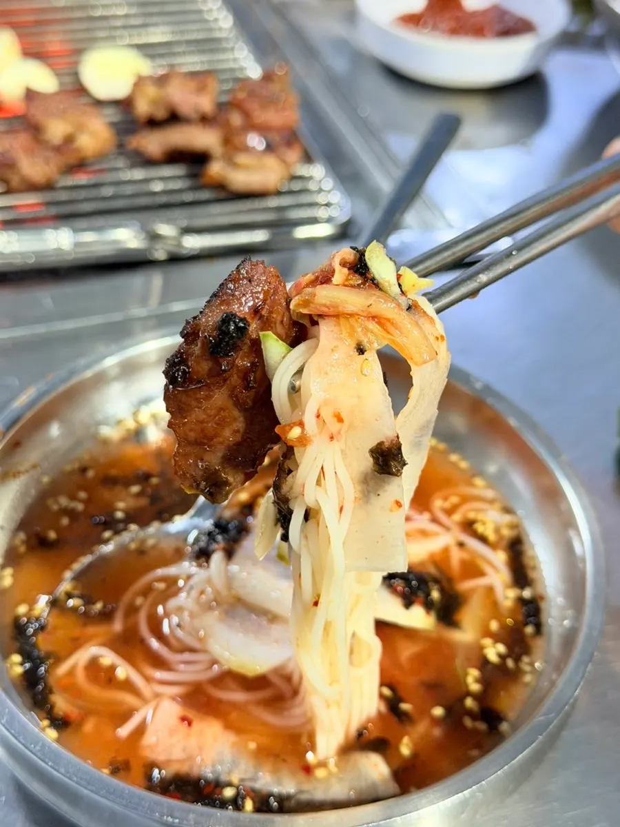 Noodles from the kimchi mari guksu lifted with chopsticks