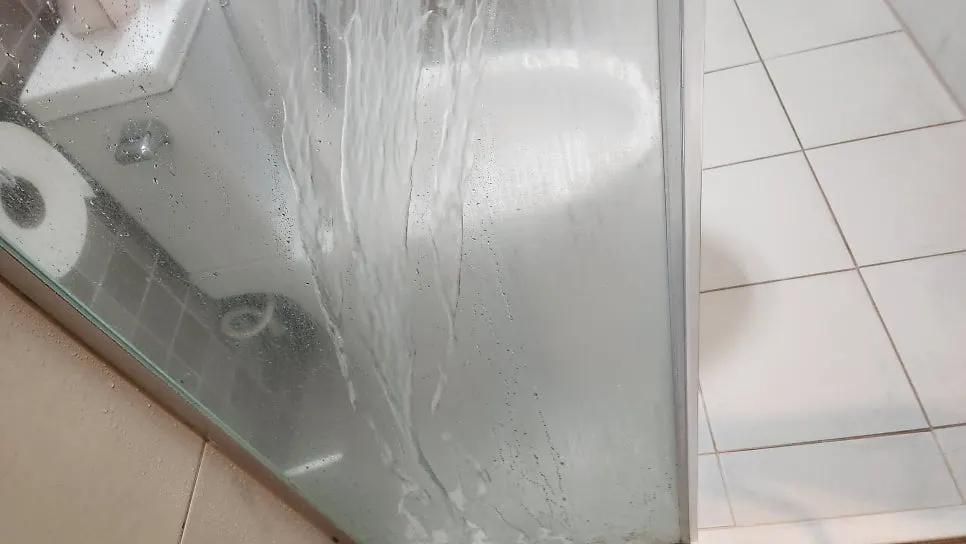 Applying film remover to wet shower glass