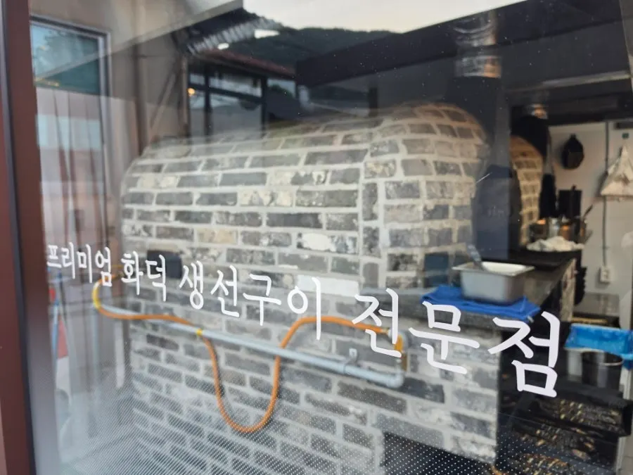 Fish being grilled in the wood-fired oven behind a glass wall