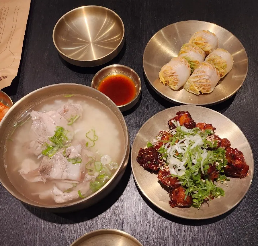 Full table spread of pork gomtang, spicy pig tail, and cabbage mandu