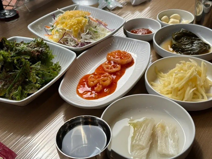 Table of banchan including lettuce salad, lotus root, and baek-kimchi