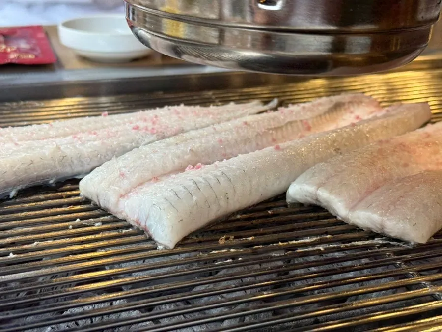 Thick eel flesh being grilled with pink salt sprinkled on top