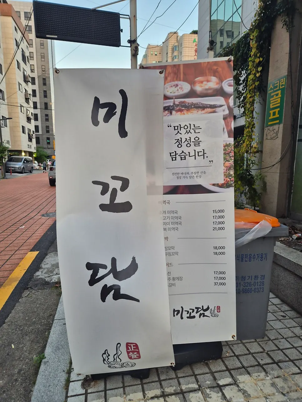 짙은 녹색 외관과 세로 입간판이 있는 미꼬담 입구