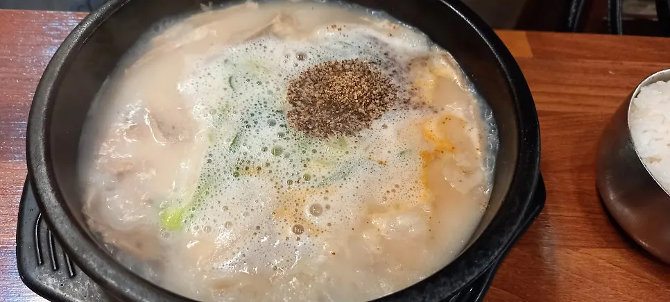 An earthenware bowl of spicy sundae gukbap with red broth, sundae, and meat