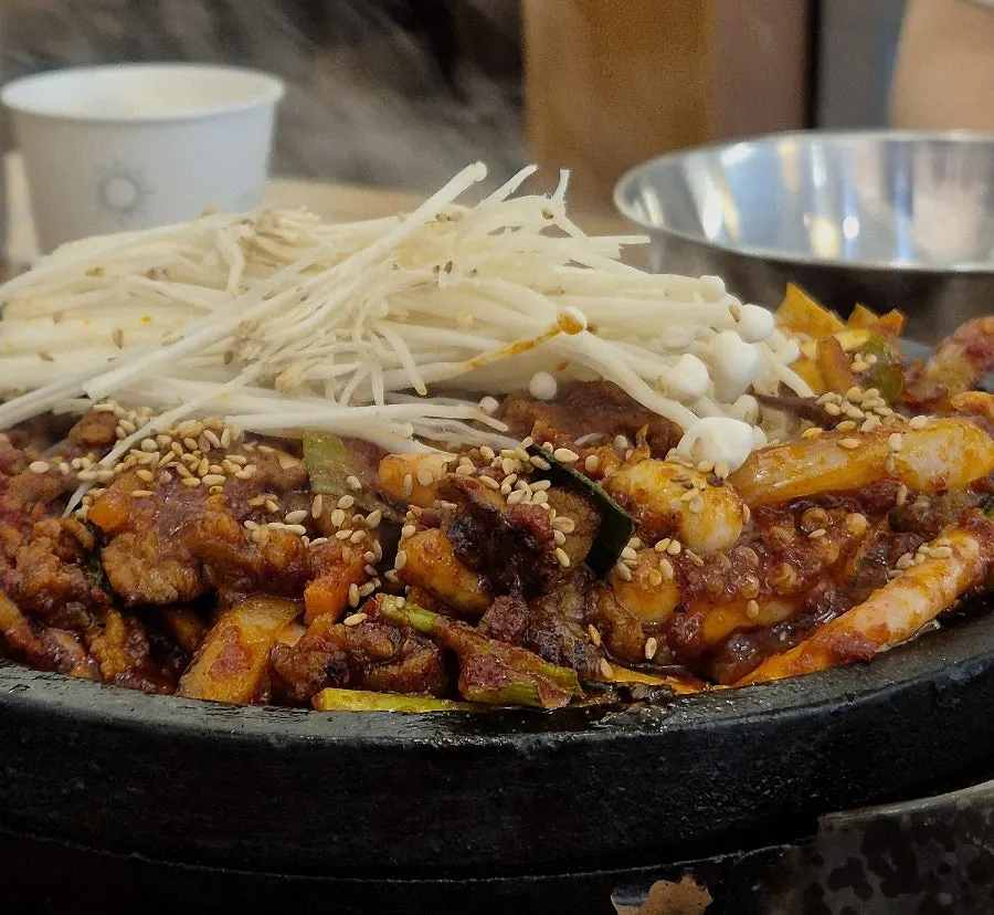 Fire-grilled squid pork stir-fry piled with enoki mushrooms on a stone plate