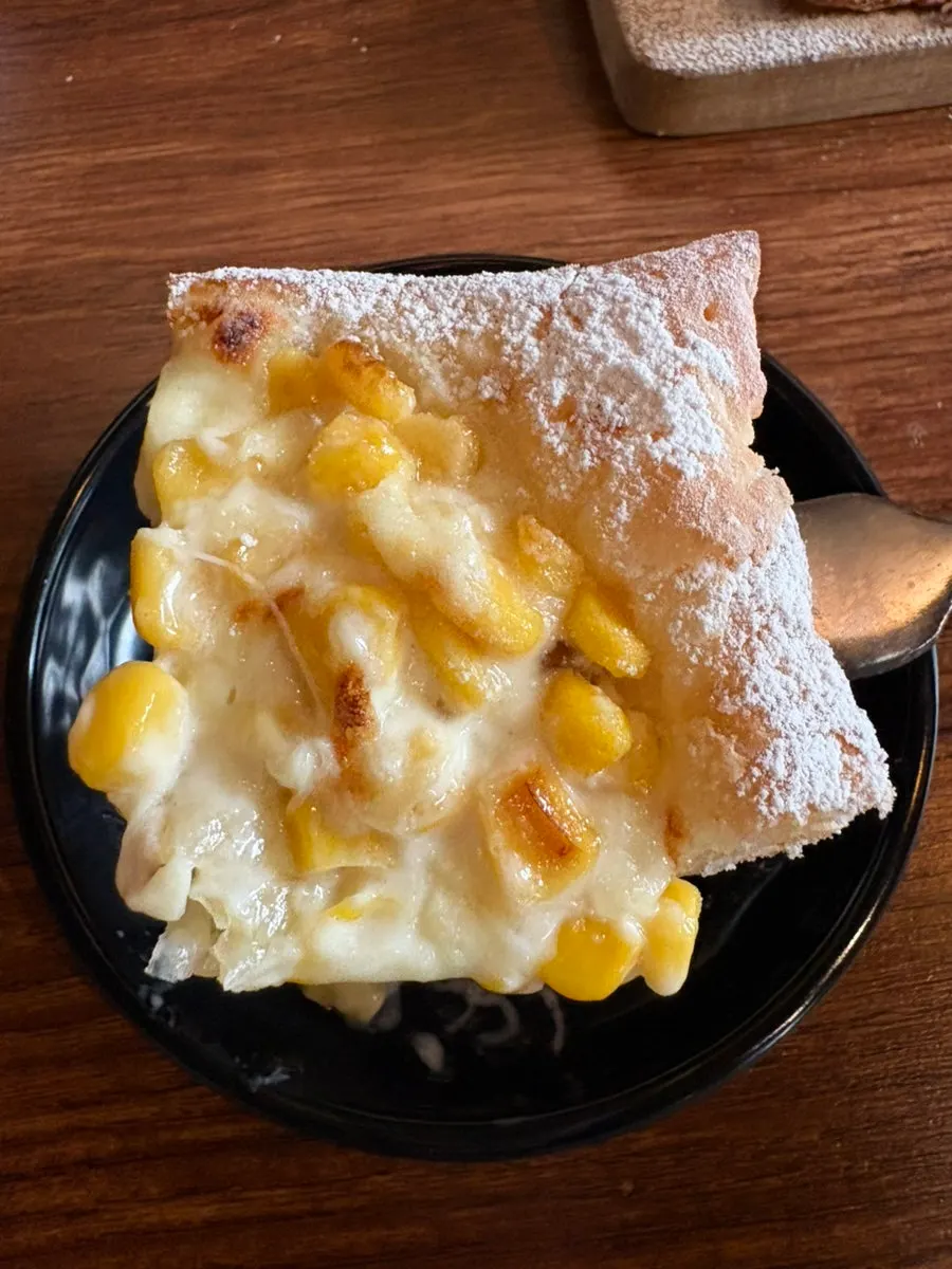 A slice of corn cheese pizza with cheese and corn toppings