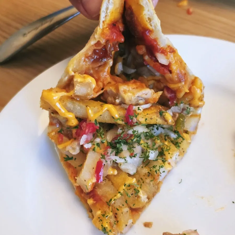 A pizza slice with potato and chicken toppings about to spill over