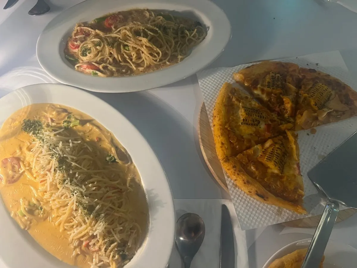 Full table shot of corn pizza and two plates of pasta