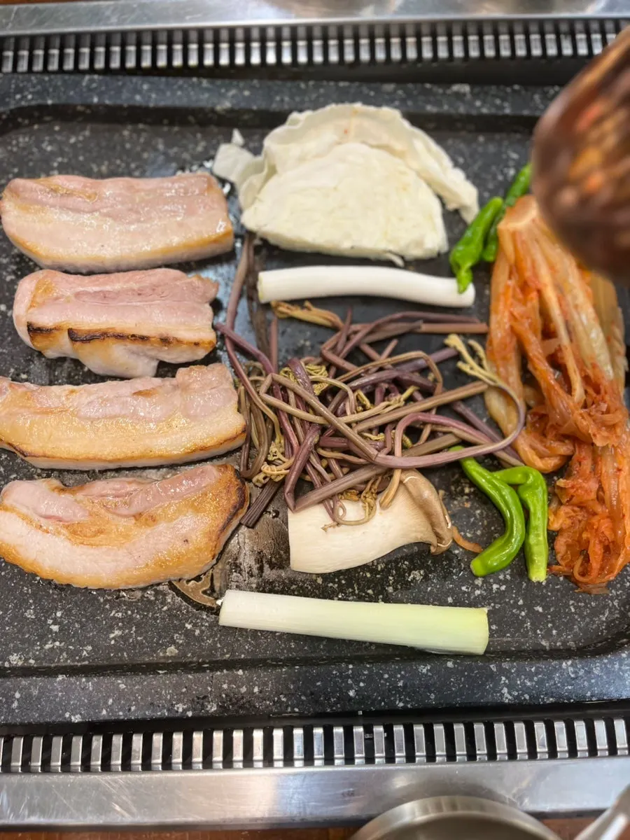 Bracken fern and aged kimchi cooking alongside the pork belly