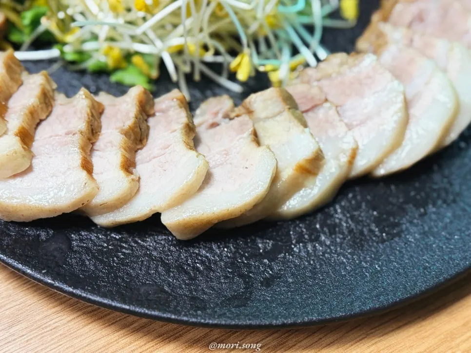 A plate of suyuk pork served with buckwheat sprouts and side dishes