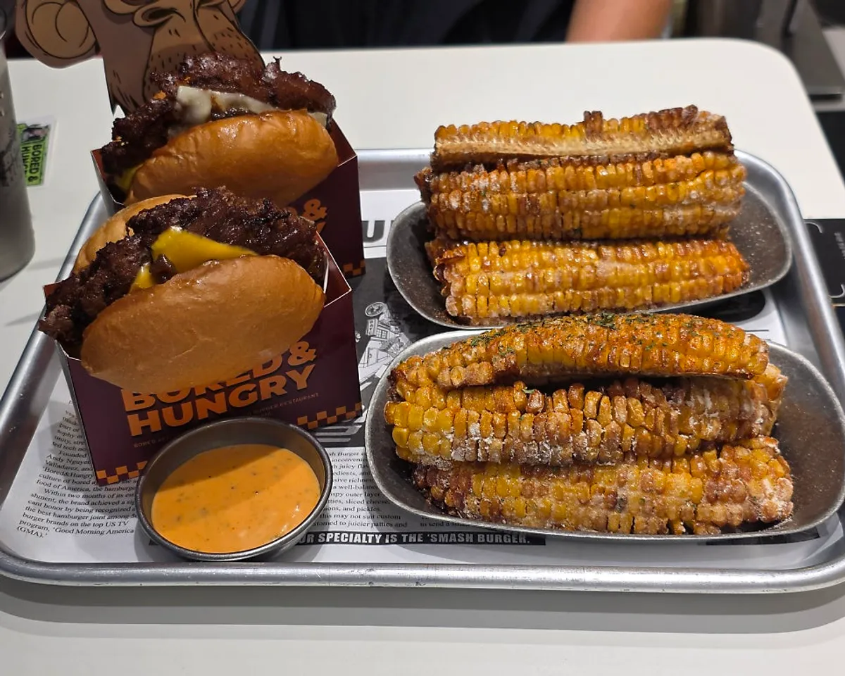 Table with two burgers and two plates of corn ribs