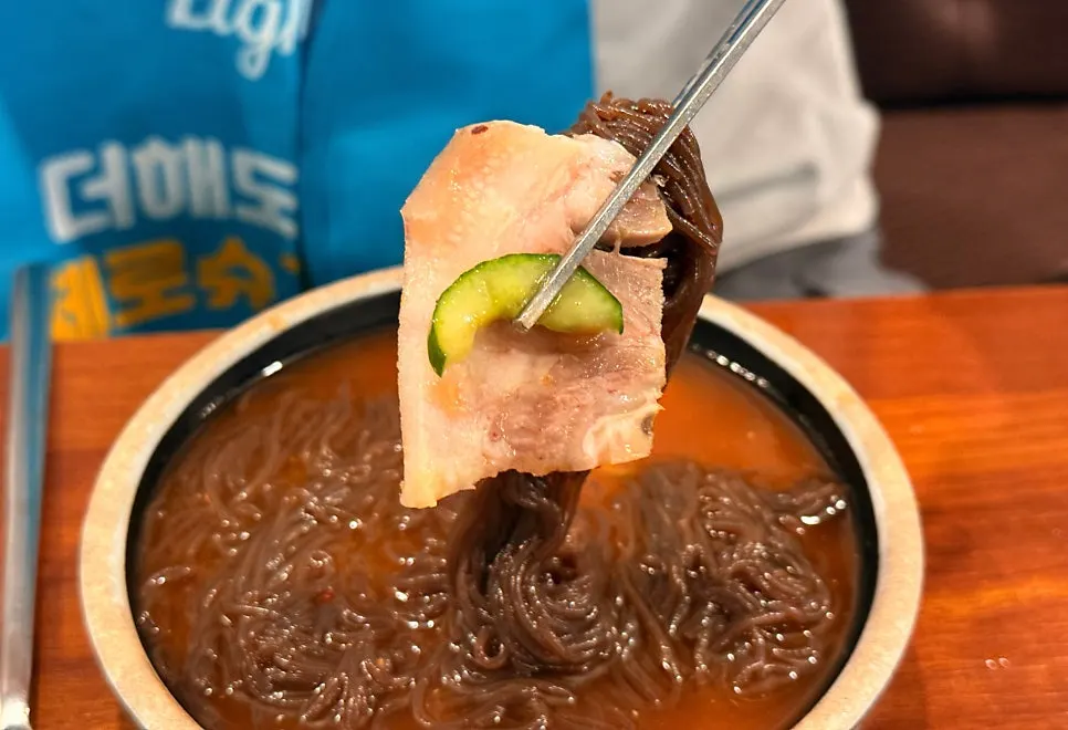 Wrapping sliced pork and cucumber with naengmyeon noodles