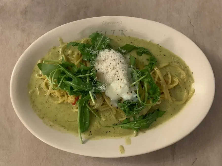 Basil pesto cream pasta topped with poached egg and rocket