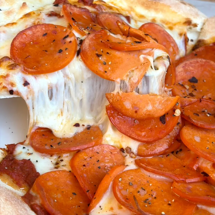 A slice of pepperoni pizza with hot sauce drizzled on top