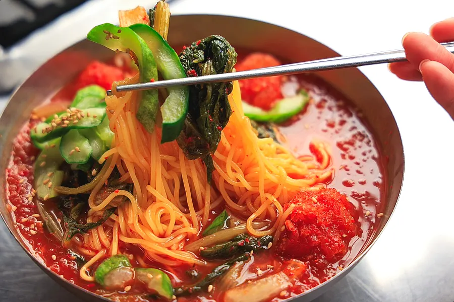 Kimchi noodle soup topped with young radish kimchi and cucumber