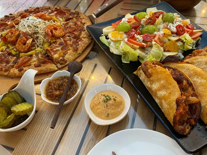 Table filled with pizza and bulgogi taco fruit salad