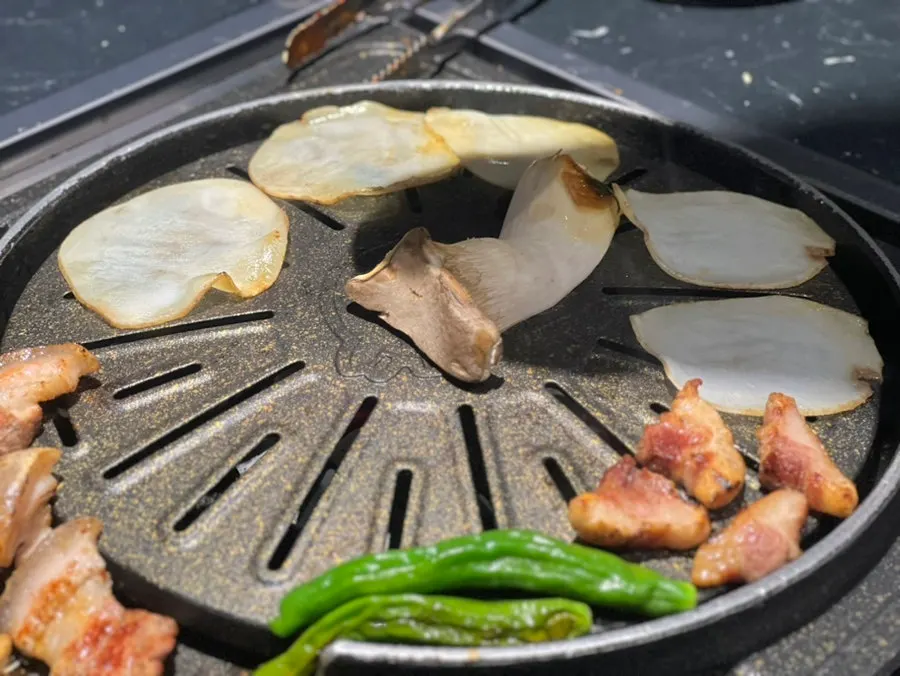 Meat set aside on the edge of the grill while potato and mushroom cook