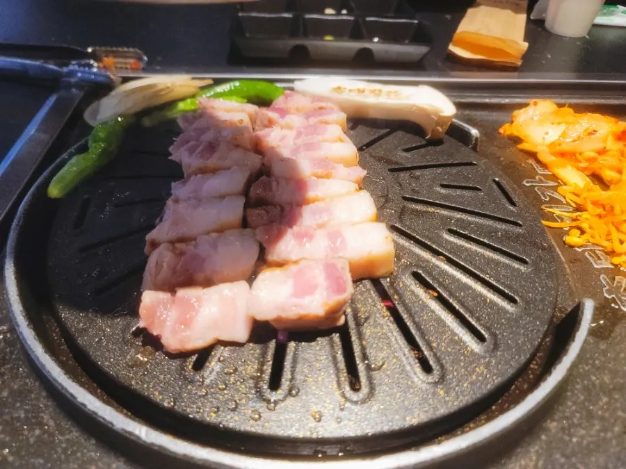 Pork belly, kimchi, and bean sprouts cooking on the grill