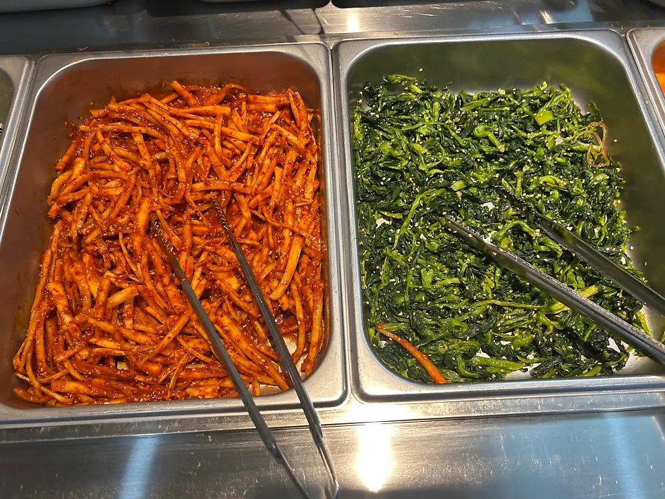 Self-bar side dishes including seasoned spinach, lotus root fritters, and japchae