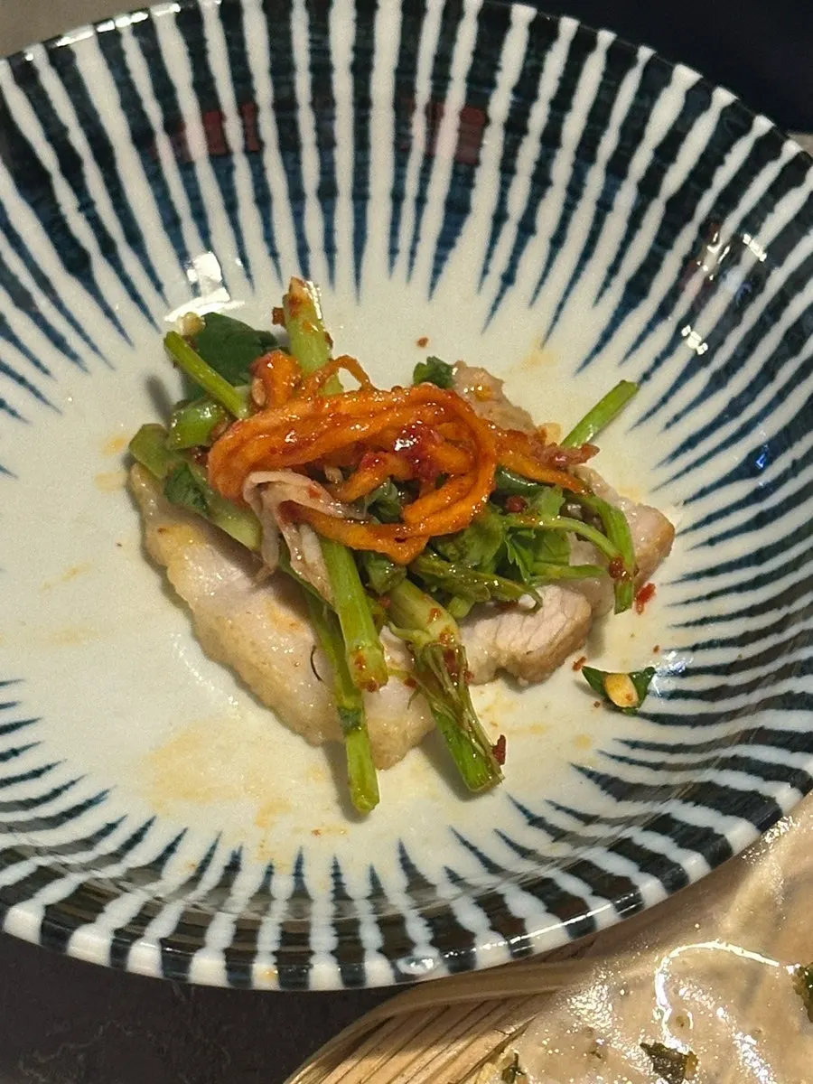 A bite of bossam topped with minari salad and dried radish strips