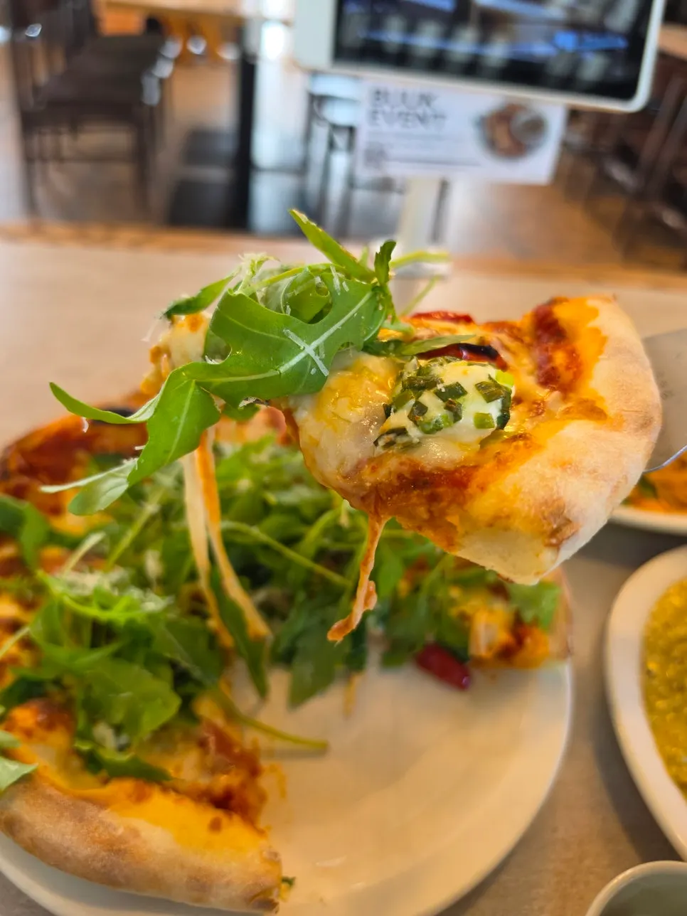 A slice of rocket prosciutto pizza with hot sauce