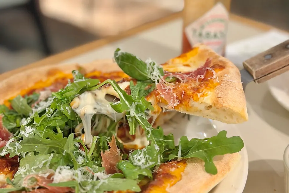 Cross-section of pizza dough topped with arugula and prosciutto